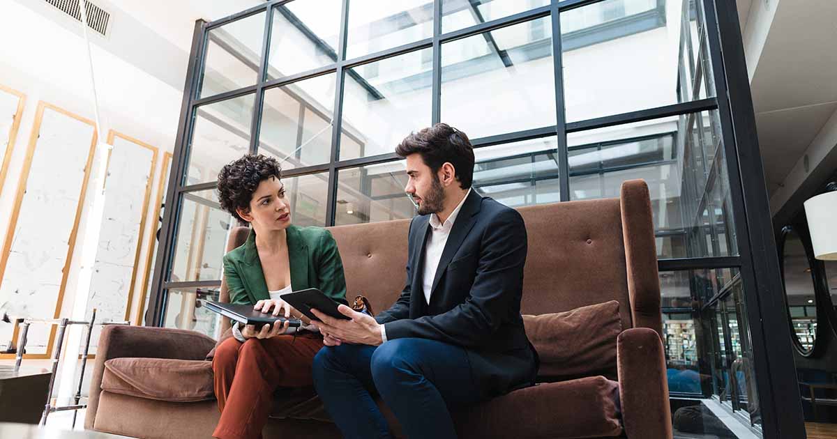 A business man and woman talking on a couch.