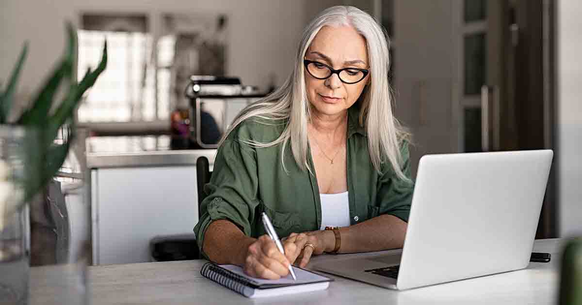 Businesswoman at laptop and writing in notepad.