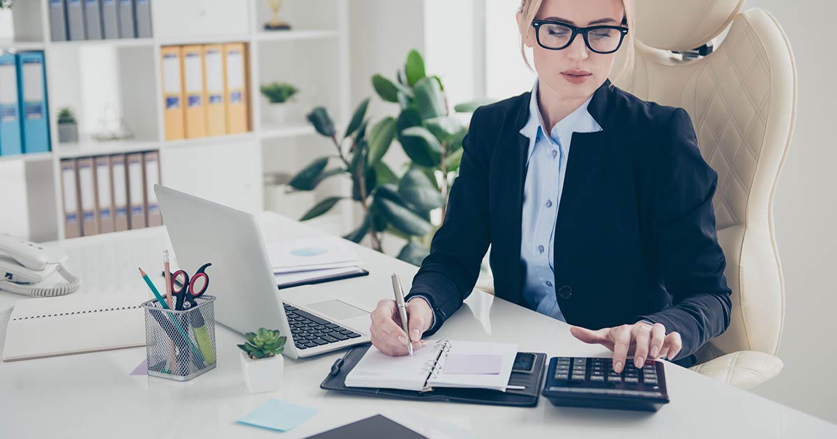 Businesswoman typing on calculator and writing in notebook.